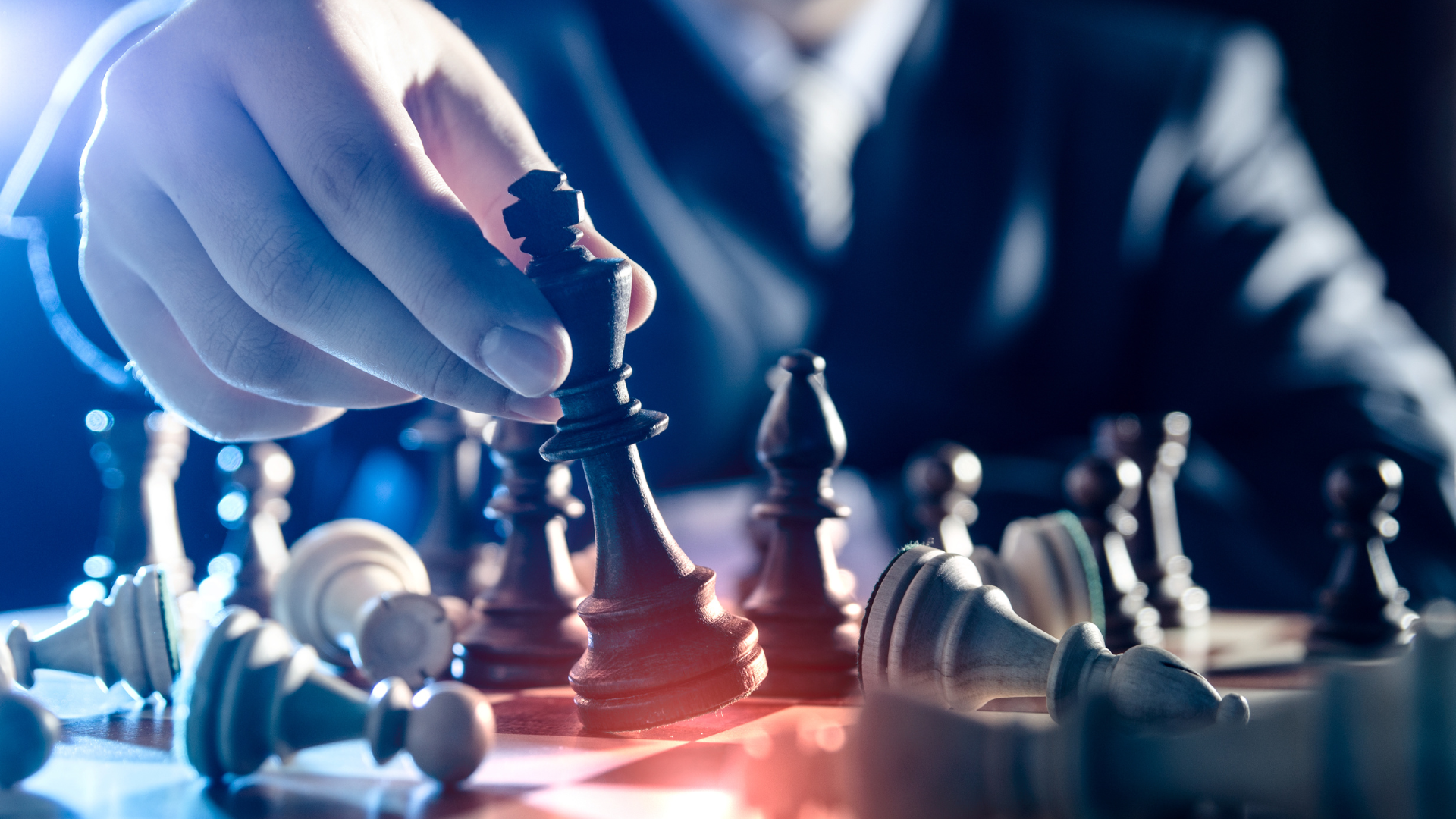 Main d'une personne en costume déplaçant une pièce d'échecs (un roi) sur un échiquier, illustrant la stratégie et la prise de décision en milieu professionnel.